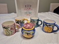 Group shot of four fruit motif mugs, sugar bowl, framed sign