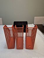 Front view of three orange mesh magazine holders and black metal file organizer