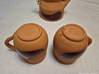 Bottoms of two cups and partial teapot showing terracotta body, glazed pepper motif, signatures visible