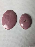 Two pink rhodonite oval cabochons on white background