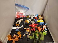 Overview of the mixed toys spread out including action figures, figurines, dinosaur and green monster, plus bag of Monopoly parts
