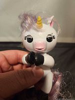 Front view of white Fingerlings unicorn on hand showing face, horn, mane, black hooves