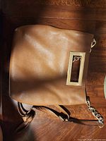 Full view of brown Michael Kors purse with chain strap on wooden surface