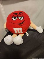 Front view of red M&M plush showing face, m logo, limbs