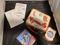 Outer cardboard sleeve, metal Slamwich tin with handle and clasp, instruction sheet, thank you note