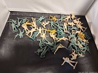 Wide view of mixed green, tan, yellow plastic army men scattered on black surface