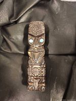 Front view of carved tiki figure showing facial features and inlaid eyes