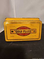 Front view of yellow Gold Flake Honey Dew cigarette tin showing graphics and registered number