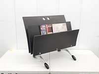 Front view showing three black wood panels, magazines for scale, silver metal legs with black feet