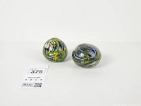 Two multicolor swirl glass paperweights front view with lot tag