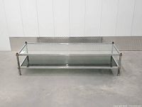 full frontal view of rectangular chrome and brass coffee table with glass top and shelf