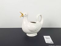 Left profile of white ceramic swan pitcher showing tail handle and embossed feathers
