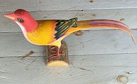 Side view of painted wooden golden pheasant sculpture on log base