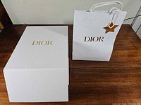 Rigid white Dior gift box and matching white paper gift bag with gold logos; star tag attached to bag
