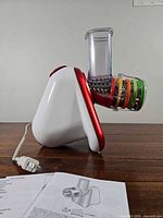 Side view of appliance with feed chute, stacked color-coded drum attachments, power cord and manual