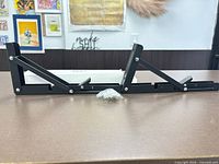 Two black folding brackets and bag of screws displayed side by side