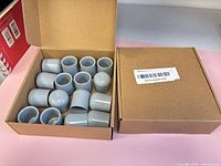 Both cardboard boxes, one open showing contents of grey caps