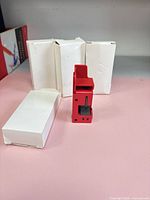 Front view of one red lockout device standing beside three unopened white boxes