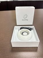Smart ring seated in charging cradle inside open box, closed box behind
