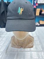 Front view of black Tentree hat showing embroidered sasquatch and tree graphic
