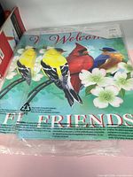 Both packaged Evergreen Welcome Friends garden flags showing bird design through clear plastic