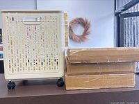 Assembled beige perforated rolling basket beside two sealed cardboard boxes