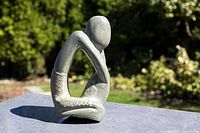 Front angle of abstract soapstone seated man sculpture outdoors