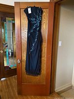 Front view of black gown with blue floral pattern hanging on door, tag visible