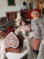 Overall view of wicker trunk filled with dolls, chair, heart-shaped box, linens