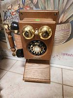Front view of wooden wall-mount rotary telephone with brass bells and black receiver