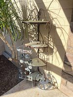 Full view of corner plant stand with glass shelves and both metal outdoor signs