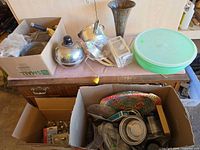 Overview of mixed kitchen items, metal vase and plastic carrier on cedar chest