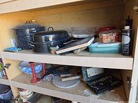 Two shelf cabinet showing enamel cookware, glass bowl, plastic storage container, jar of screws, spray bottle, ceramic bowl, candlesticks, tools, marble board, drill bit set