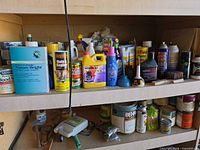 Two garage shelves filled with paint cans, aerosol cans, chemical bottles and small tools