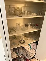 Closet shelves with varied clear glassware and linens below