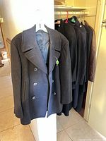 Closet view showing multiple dark coats including pea coat and other overcoats