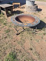 Full view of round fire pit showing tile rim, metal bowl, wrought iron legs