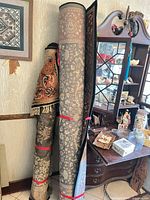 Two rolled rugs, one grey/beige floral, one orange/black accent