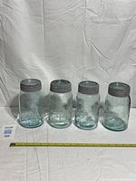 Front view of four aquamarine Crown mason jars with lids lined up, measuring tape in foreground