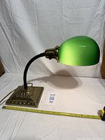 Side view showing green shade, gooseneck, brass base, tape measure for scale