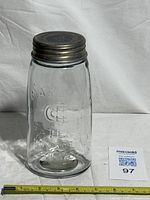 Front view of embossed clear glass Mason jar with threaded metal lid and ruler for scale