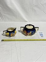 Sugar bowl with lid and creamer side by side with measuring tape for scale