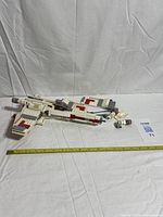 Wide shot of partially assembled X-wing with loose pieces and measuring tape for scale