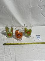Front view of three daisy juice glasses beside tape for scale