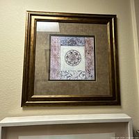 Overall view of square framed print on wall showing frame, mat and artwork