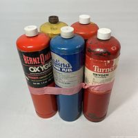 Front view of all five metal gas cylinders strapped together showing brands and colours