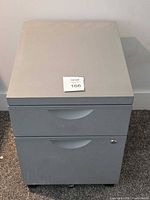 Front view of grey 2-drawer file cabinet showing overall condition and lot sticker