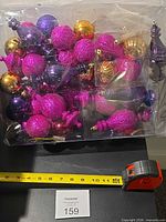Bag filled with various coloured plastic ornaments, tape for scale
