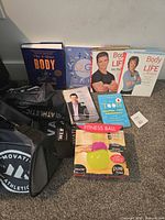 Group shot: six fitness books, Pure Fitness ball box, Innovative Athletic duffel on carpet