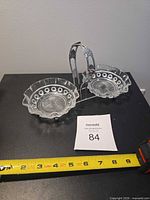 Twin pressed glass bowls in metal caddy with handle shown alongside measuring tape